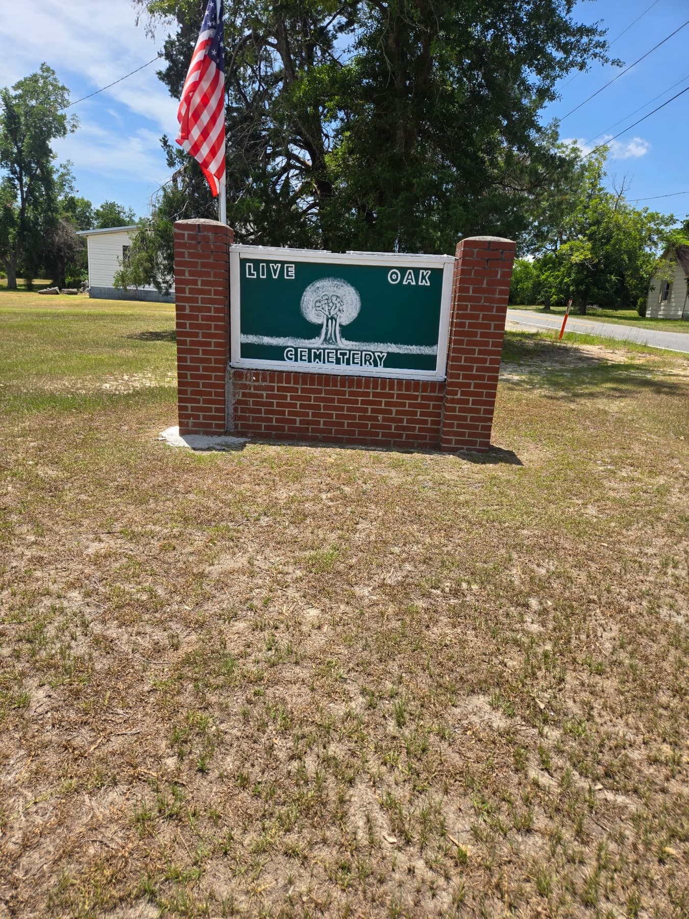 The hand-painted Live Oak Cemetery sign on brick pillars, the American flag above
